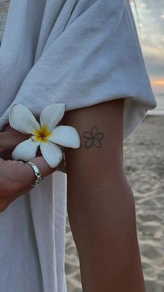 a person with a flower tattoo on their arm next to the ocean and sand at sunset