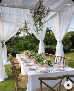 an outdoor dining area with white drapes and flowers on the table set for dinner