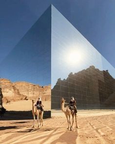 two people riding camels in front of a pyramid with the sun shining on it