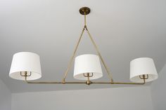 a chandelier with three white lamps hanging from it's sides and one light on the other side