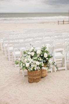 two baskets with flowers are sitting on the sand near an empty chair at the beach