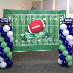 balloon arch with football balloons on it in front of a green and white field backdrop