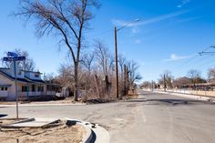 an empty street with no cars on it and trees in the foreground, next to a white building