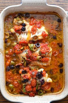 a white casserole dish filled with chicken, olives and tomatoes