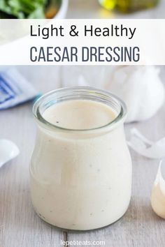 a glass jar filled with dressing sitting on top of a table next to a salad