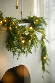 a christmas wreath with lights hanging from it's side next to a fire place