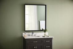 a bathroom vanity with a mirror above it and a vase on the counter next to it