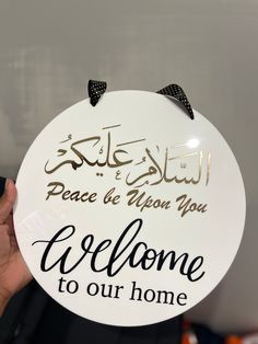 a person holding up a sign that says welcome to our home in arabic and english