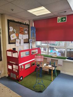 a red double decker bus sitting in front of a window next to a green rug