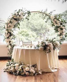 a table with white flowers and greenery on it in front of a large window