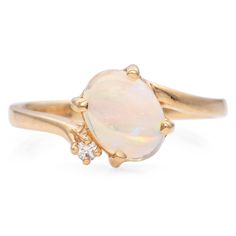 a white opal and diamond ring with two gold rings on each side, set against a white background