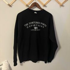 a black long sleeved shirt hanging on a wooden hanger next to a white wall