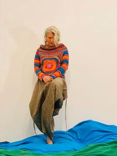 a woman sitting on top of a blue and green blanket next to a white wall