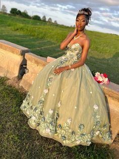 a woman in a green dress sitting on a stone wall next to flowers and grass