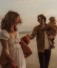 a man holding a baby while standing next to two other people on a sandy beach