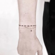 a woman's wrist with a small beaded bracelet on her left hand and an arrow tattoo on the right arm