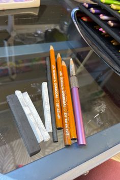 three pencils and two erasers on a glass table with other colored crayons