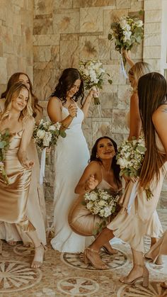 a group of women standing next to each other in front of a stone wall holding bouquets