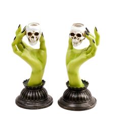 two green statues with hands holding cups in the shape of human arms and skull heads