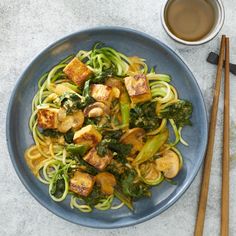 a blue plate topped with noodles and veggies next to two chopsticks