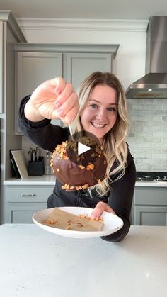 a woman holding up a chocolate donut with nuts on it