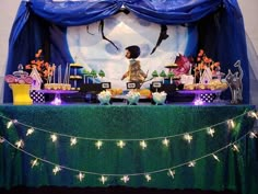 a table topped with cake and cupcakes covered in frosting next to a blue curtain