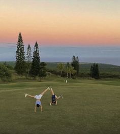 two people doing handstands in the grass on a golf course at sunset or dawn