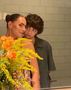 two women standing next to each other in front of a mirror with flowers on it