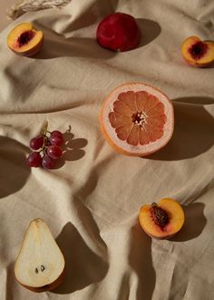 an apple, orange and grapefruit cut in half on a tablecloth with other fruit