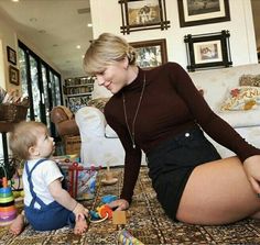 a woman kneeling down next to a baby on the floor playing with toy cars and blocks