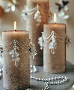 three candles are sitting on a table with beads and chains hanging from the candle holders