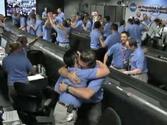 two men hugging each other in the middle of a room full of people wearing blue shirts