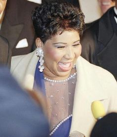 a woman in a blue dress and white jacket smiling at someone with her mouth open