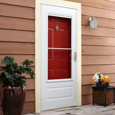 a red door on a tan house with potted plants in the foreground and a planter next to it