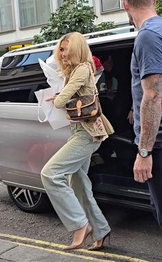 the woman is getting out of the car with her hand in her pocket and another man standing next to her