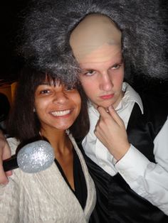 a man and woman posing for the camera with wigs on their heads in front of them