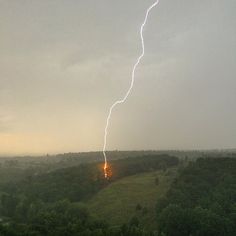 a lightning bolt is seen in the sky over a green field with trees and hills