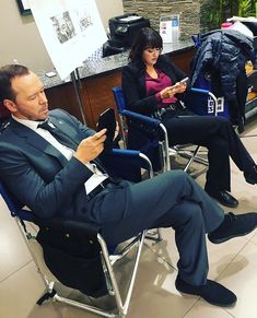 a man in a suit sitting on a chair next to a woman who is looking at her phone