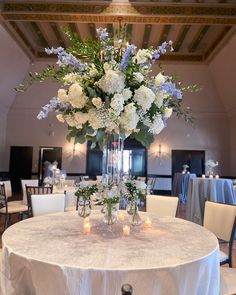 a vase filled with white and blue flowers sitting on top of a table covered in candles