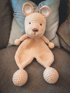 a crocheted teddy bear sitting on top of a couch next to a pillow