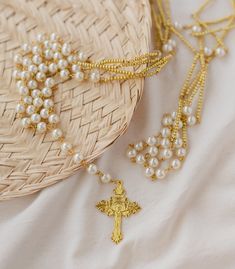 a straw hat with pearls and a gold cross on it next to a woven basket