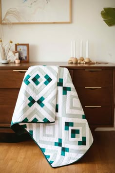 a green and white quilt sitting on top of a wooden dresser