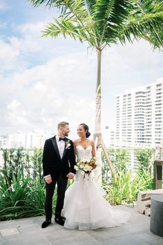 a bride and groom standing under a palm tree