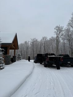 two trucks parked in front of a house on a snow covered road next to trees