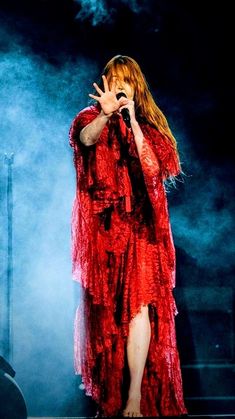 a woman in a red dress standing on stage with her hands up to her face