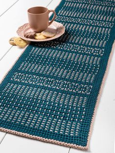 a crocheted table runner with a cup and plate on it, next to cookies