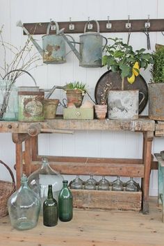 an old wooden table topped with lots of potted plants and watering cans on top of it