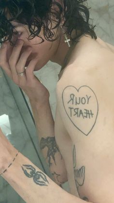 a man with a heart tattoo on his left arm holding a cell phone to his ear