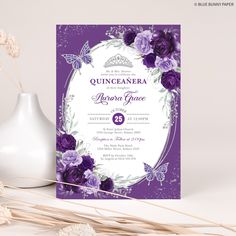 a purple and white wedding card with flowers in the middle, on top of a table