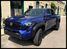 a blue toyota pickup truck parked in front of a brick building with green shutters